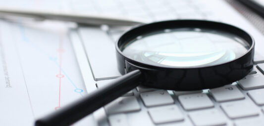 Magnifying glass lies on white keyboard on desk in office table workplace closeup.